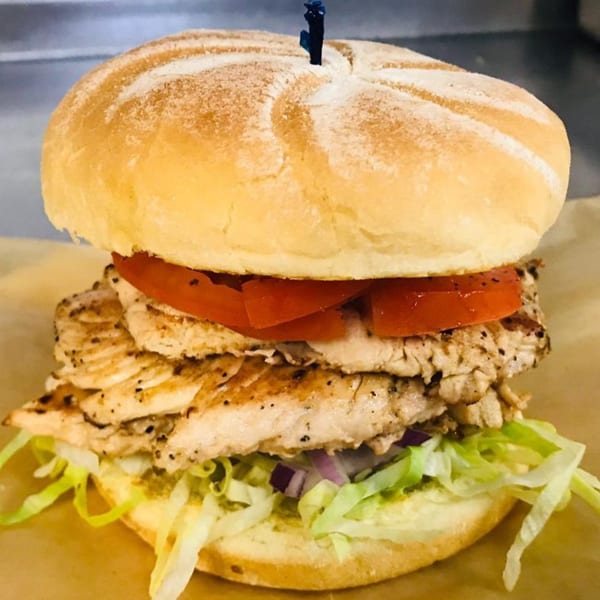Grilled chicken sandwich with lettuce, red onion, and tomato on a bun, held by a toothpick.