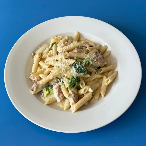 Creamy penne pasta with chicken, broccoli, and grated cheese on a white plate.