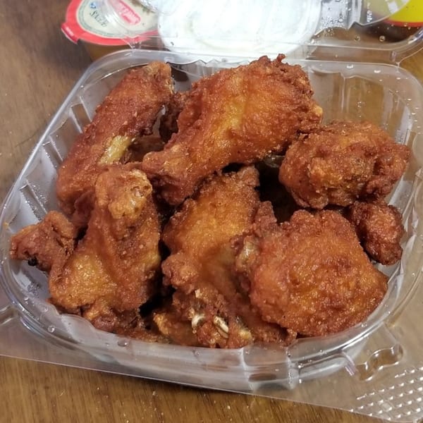 A plastic container filled with golden-brown, crispy fried chicken wings from Amore Pizza.