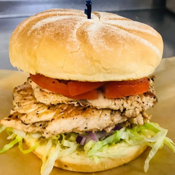 Grilled chicken sandwich with lettuce, red onion, and tomato on a bun, held by a toothpick.