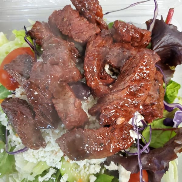 Steaming grilled steak pieces on a fresh salad with feta cheese, tomatoes, and mixed greens.