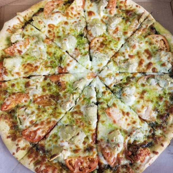 Amore Pizza's pesto pizza with melted cheese, artichoke hearts, and tomato slices, cut into eight slices.